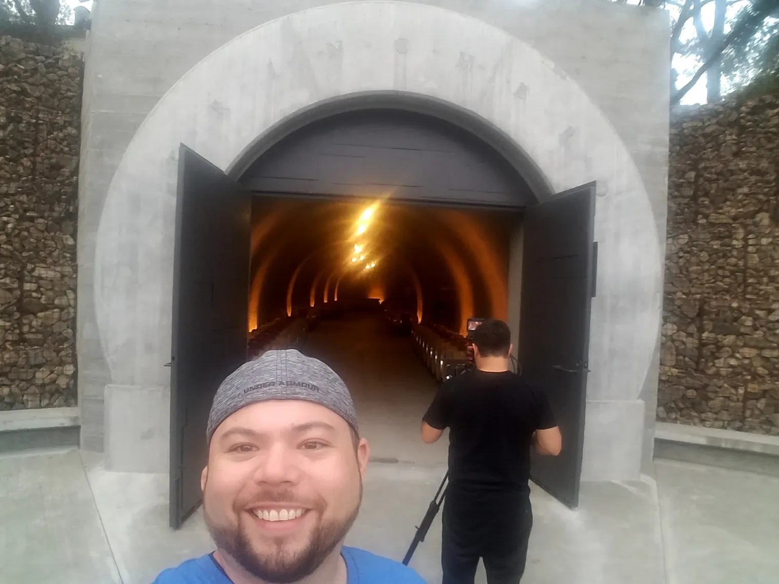 An arched concrete cellar entrance with a camera operator filming into a barrel-lined tunnel