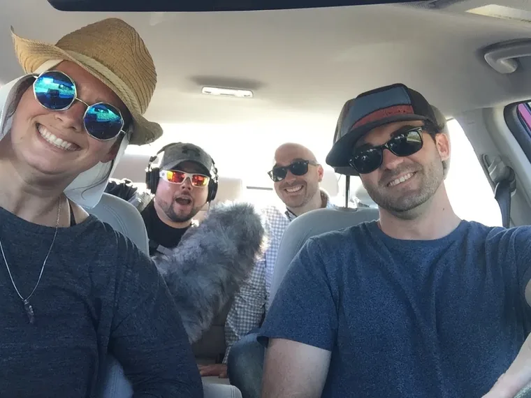 Four crew members inside a vehicle, one holding a boom microphone, all wearing sunglasses