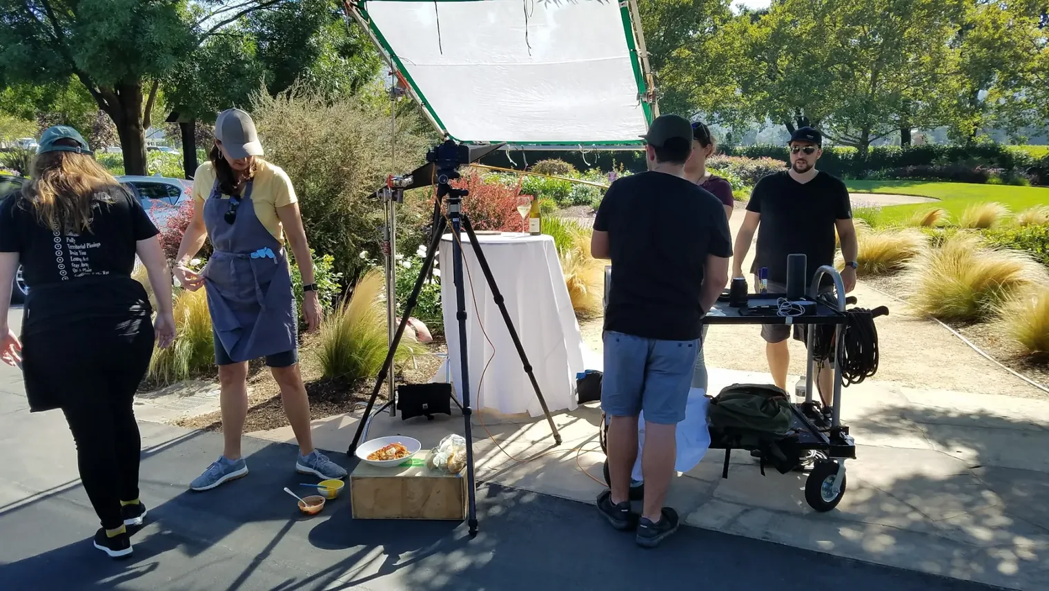Crew setting up a food and wine shot on a white-draped table under an overhead diffusion frame