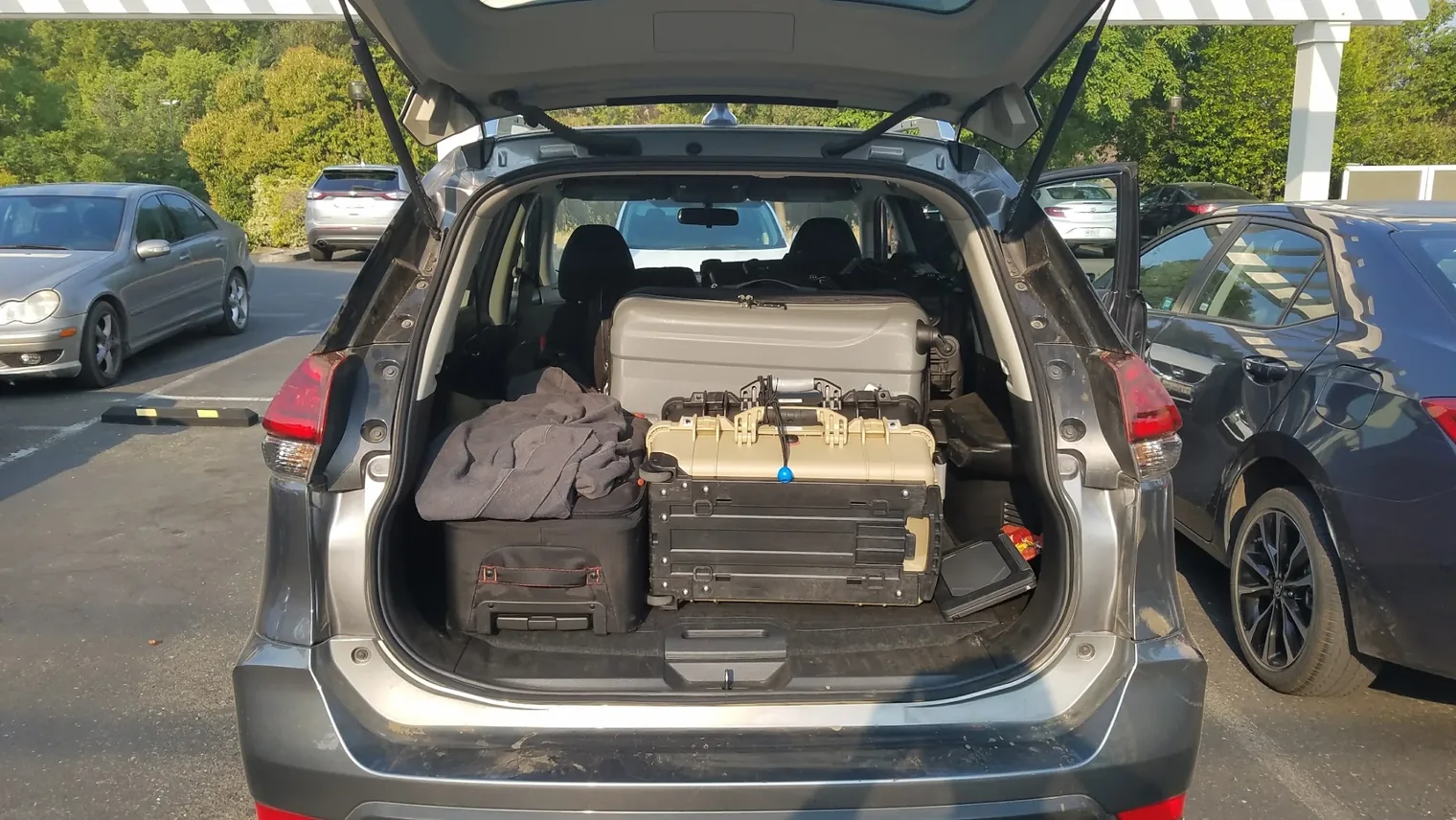 The open rear of an SUV packed with hard equipment cases and luggage in a parking lot