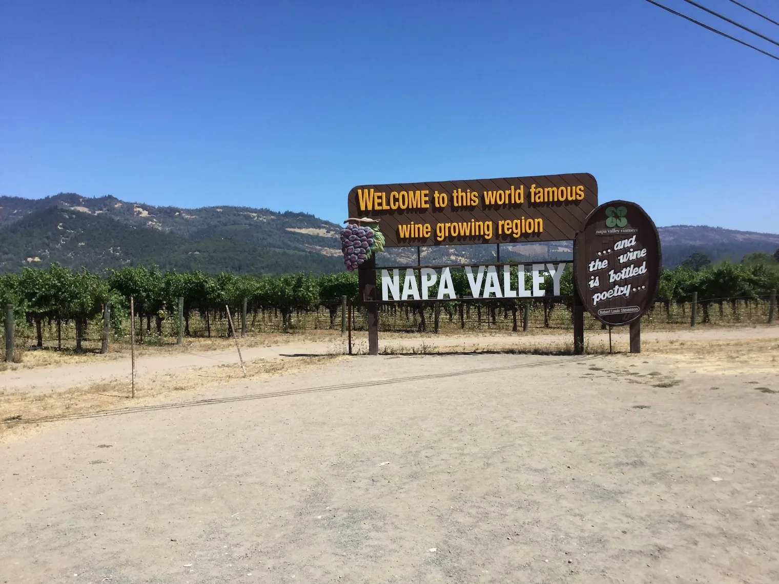 A roadside sign reading Welcome to this world famous wine growing region, Napa Valley, with vine rows behind it