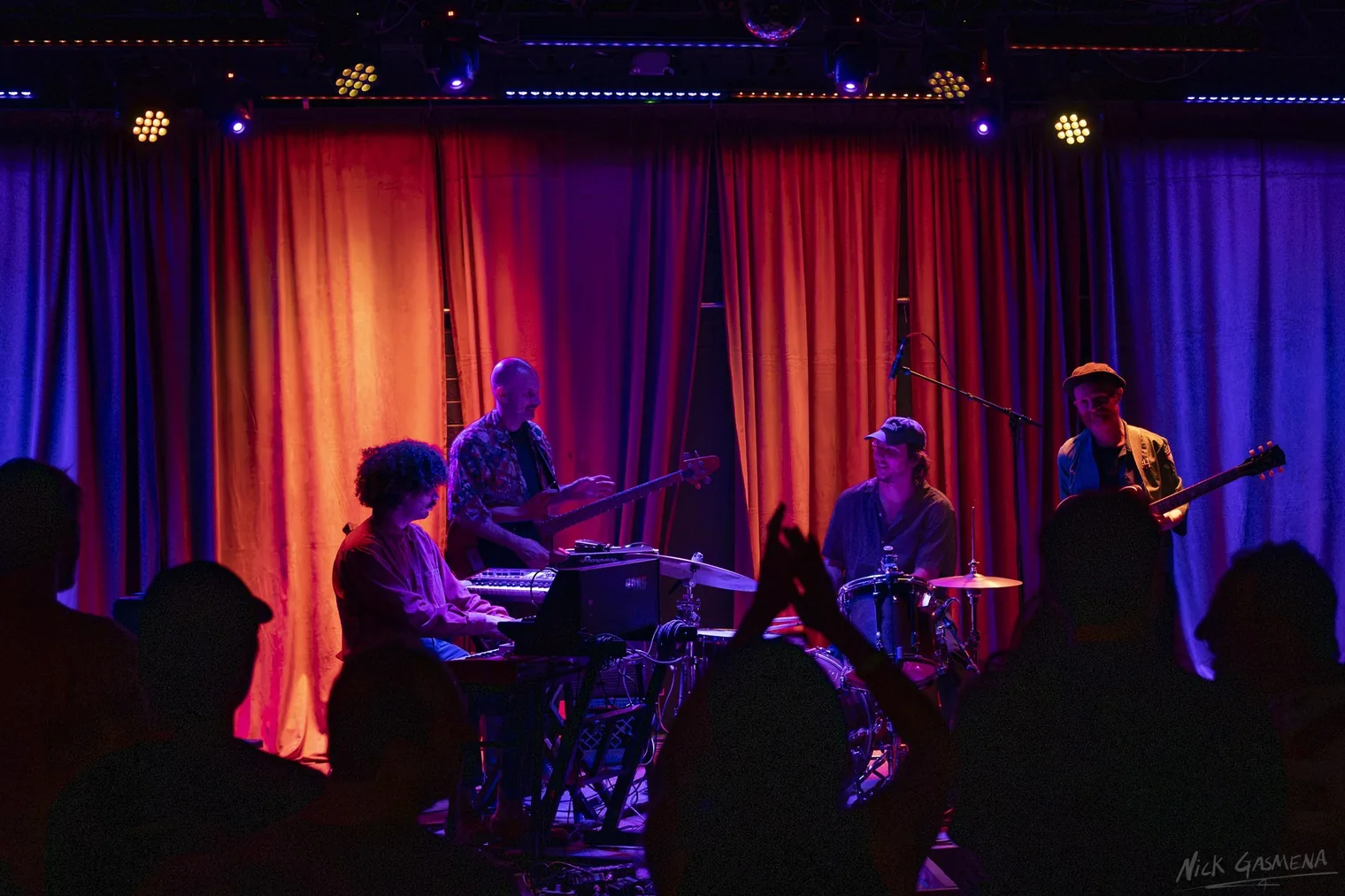 Silhouetted audience members stand close to the stage in a dark room at The Rosetta Room.