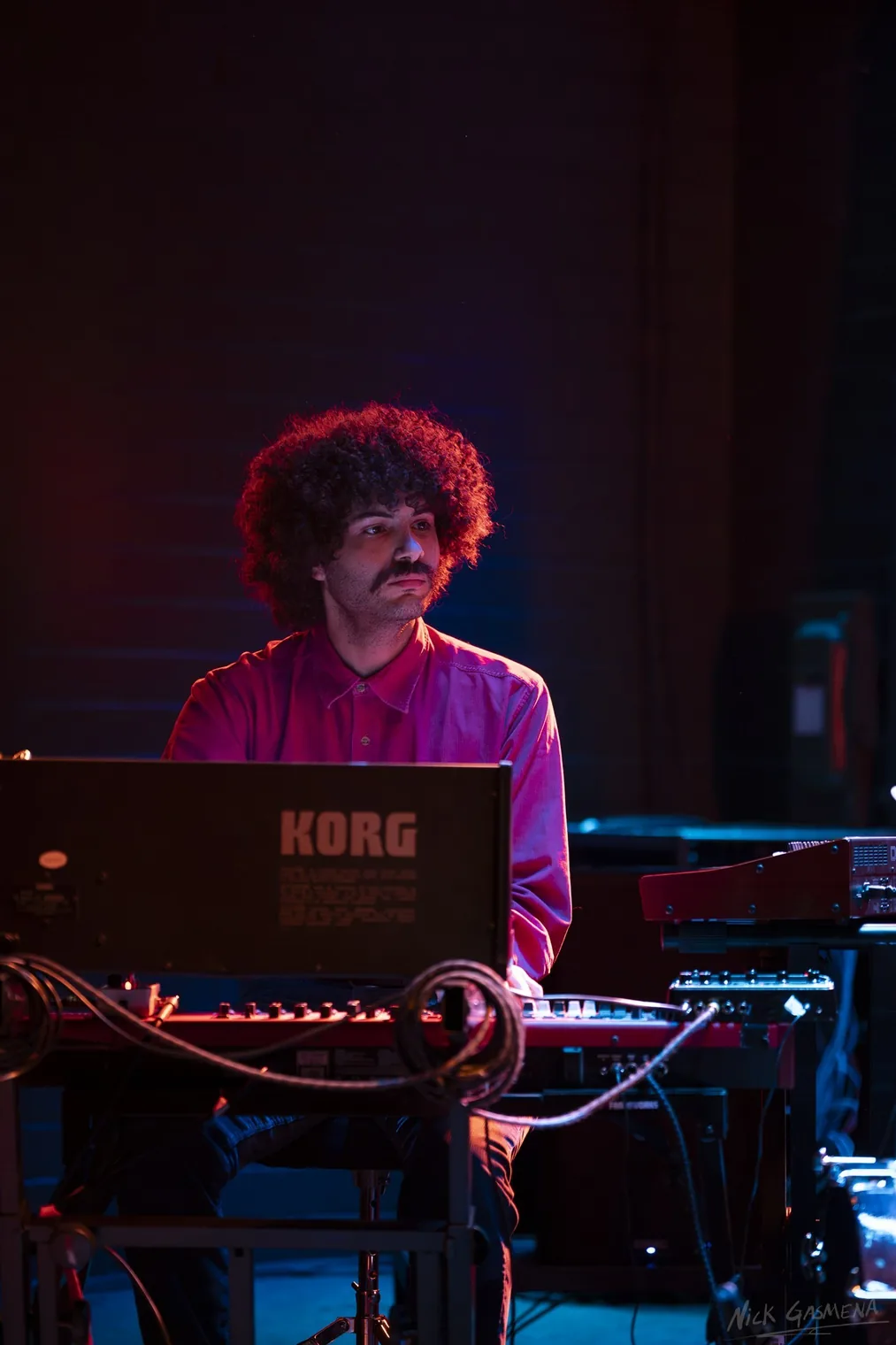 Eitan Drabkin leans over an electric piano and KORG keyboard under magenta stage light.