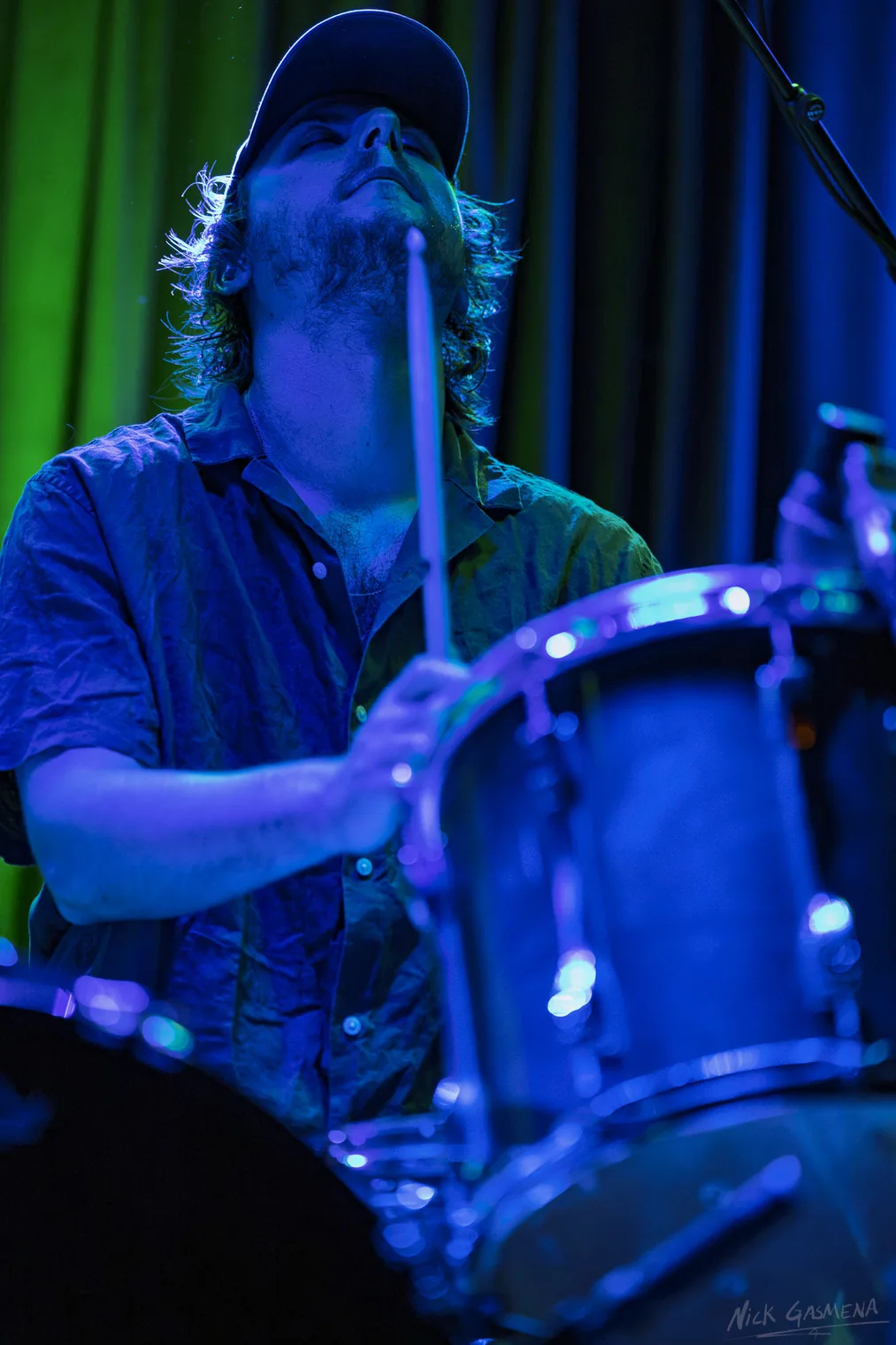Itamar Weinstein plays a drum kit under blue stage light.