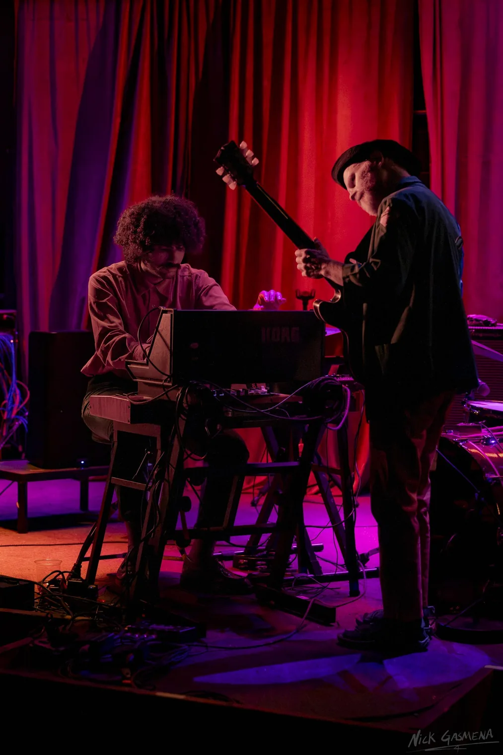 Eitan Drabkin plays keys while Ilan Smilan stands behind him in front of a red stage curtain.