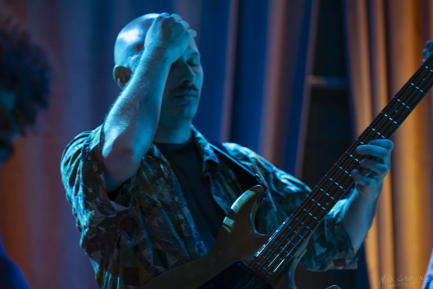 Amir Sadot plays bass guitar in close-up under blue stage light.
