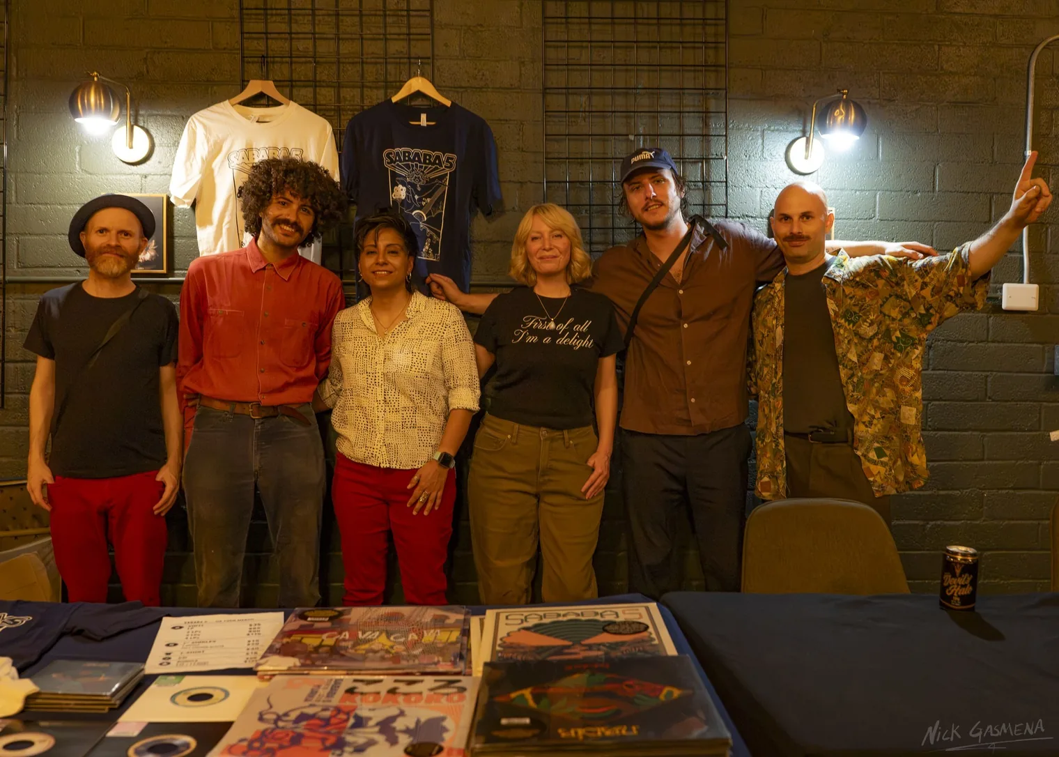 Members of Sababa 5 stand with two friends at a merchandise table of records and shirts.