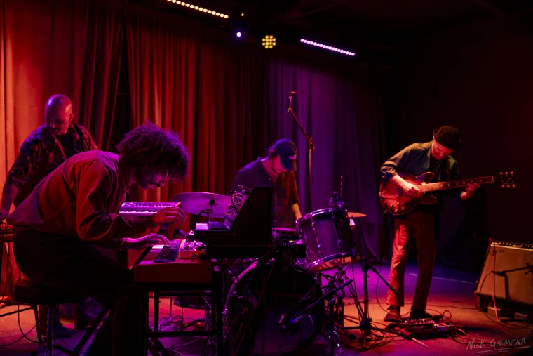 Sababa 5 playing under red and magenta light, Drabkin leaning over the keys at left and Sadot on bass at right